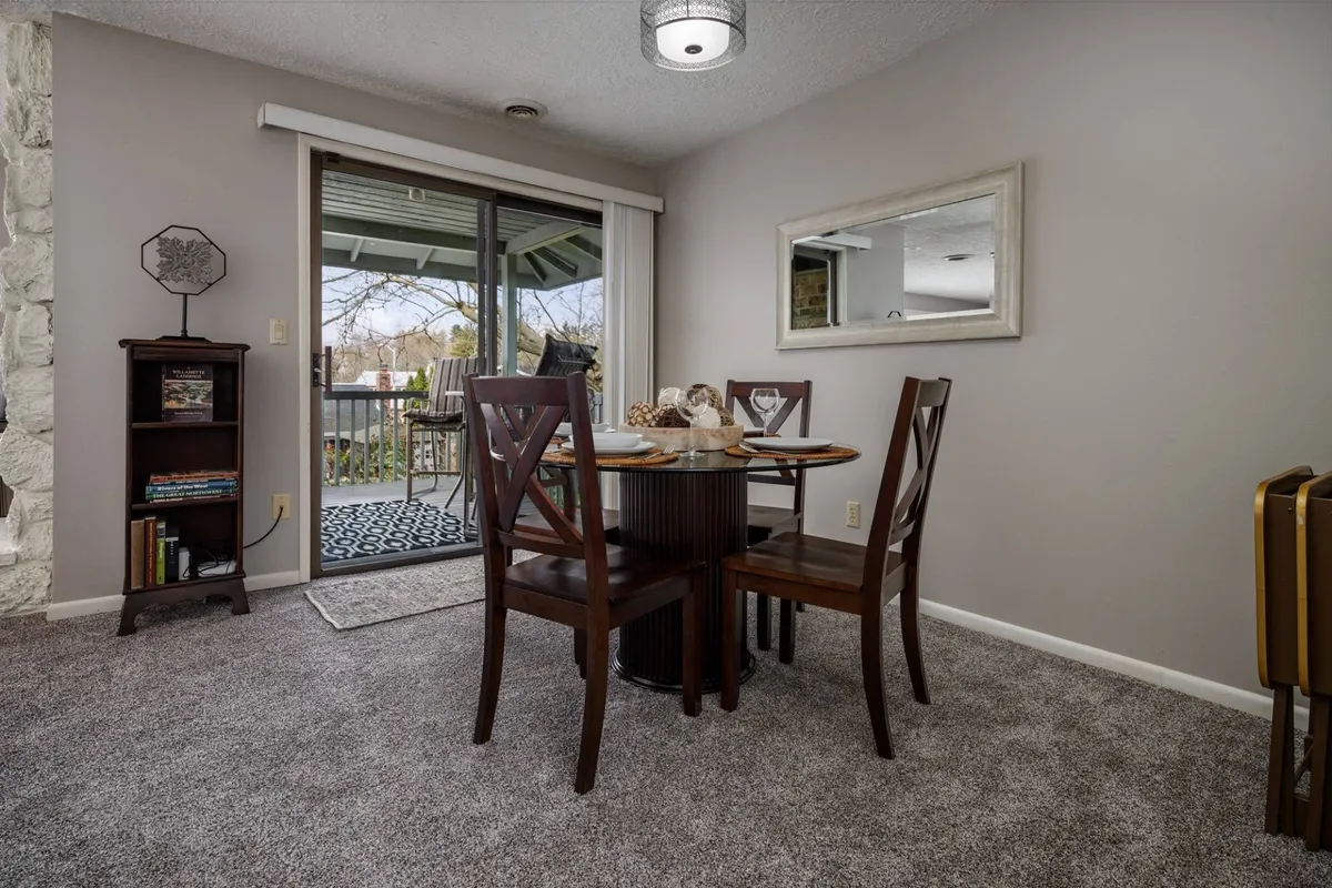 A welcoming dining area anchored by a stylish table, positioned near a sliding glass door that brings in natural light. A bookshelf adds personality and comfort to the space, suggesting moments spent enjoying meals, coffee, or quiet reading.