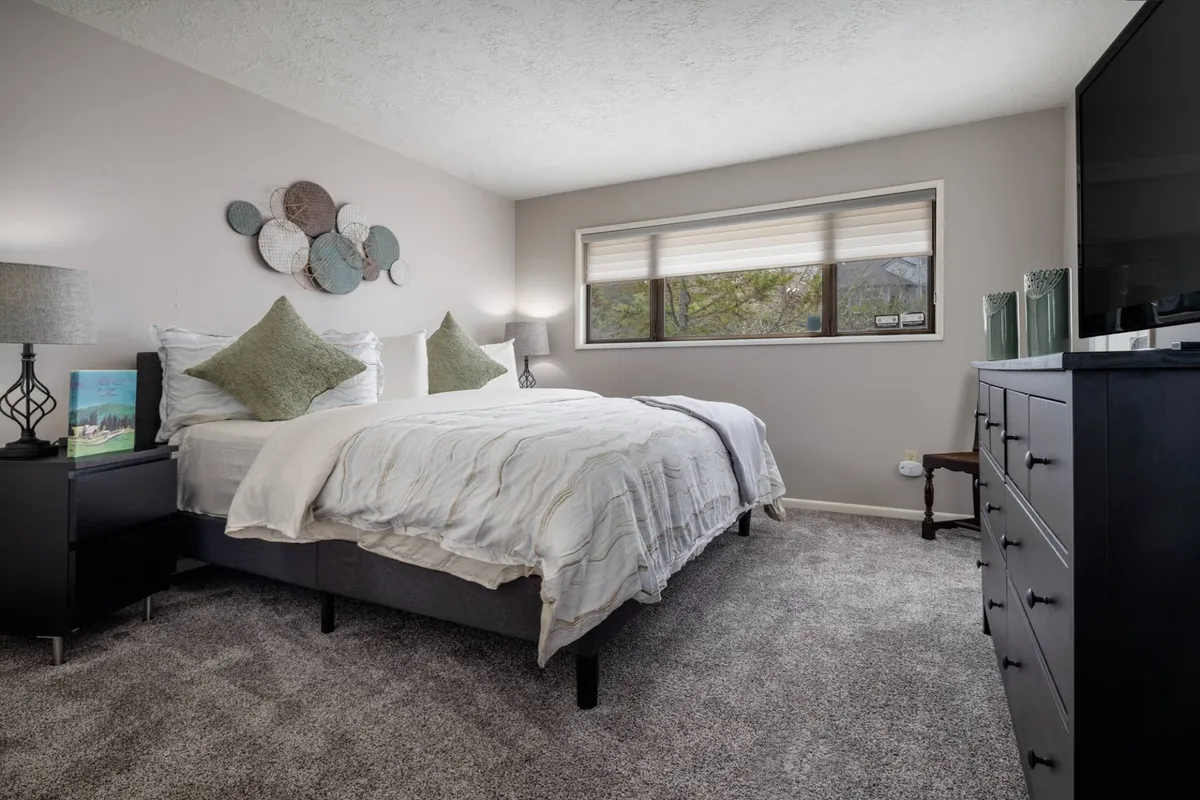 A tranquil bedroom featuring a plush king bed as its main focal point, complemented by decorative wall art, matching nightstands, and a television. Natural light streams through the window, enhancing the calm, restful atmosphere—ideal for relaxing after a day of adventure.