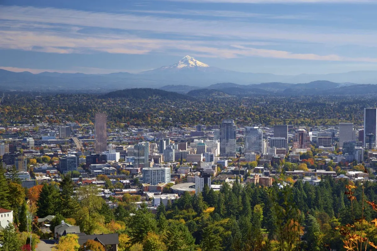 A panoramic view with lush greenery in the foreground, the downtown Portland skyline, and Mount Hood rising in the background. The scene captures the inviting, nature-rich surroundings near the property, echoing the Pacific Northwest setting.