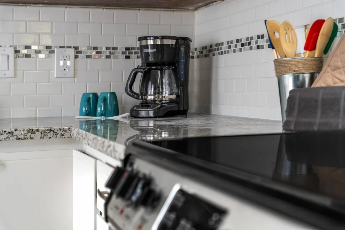A functional kitchen corner featuring a coffee maker atop a granite countertop, surrounded by colorful mugs and essential utensils. The setup evokes both daily rituals and social interactions in the kitchen.