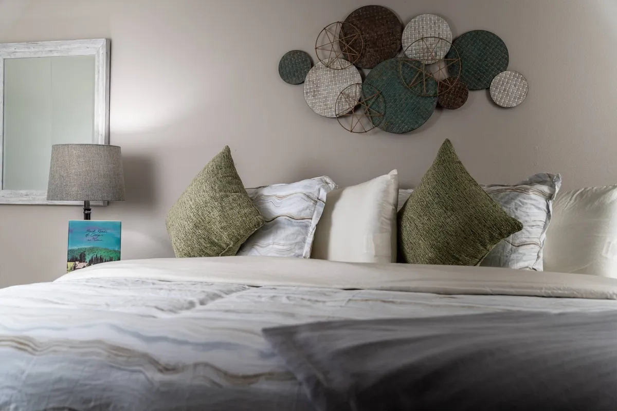 A bedroom scene showcasing a well-made bed with plush pillows, a nightstand with a warm lamp, and tasteful wall art. The natural lighting and organized setup evoke calm and restful vibes.