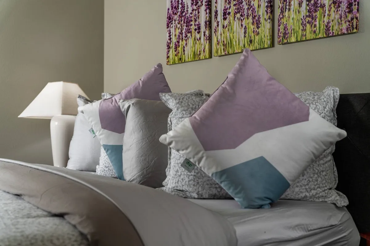 A serene sitting area featuring decorative pillows, lavender-themed artwork, and a softly glowing table lamp. The space invites quiet moments, perfect for reading or enjoying a relaxing coffee.