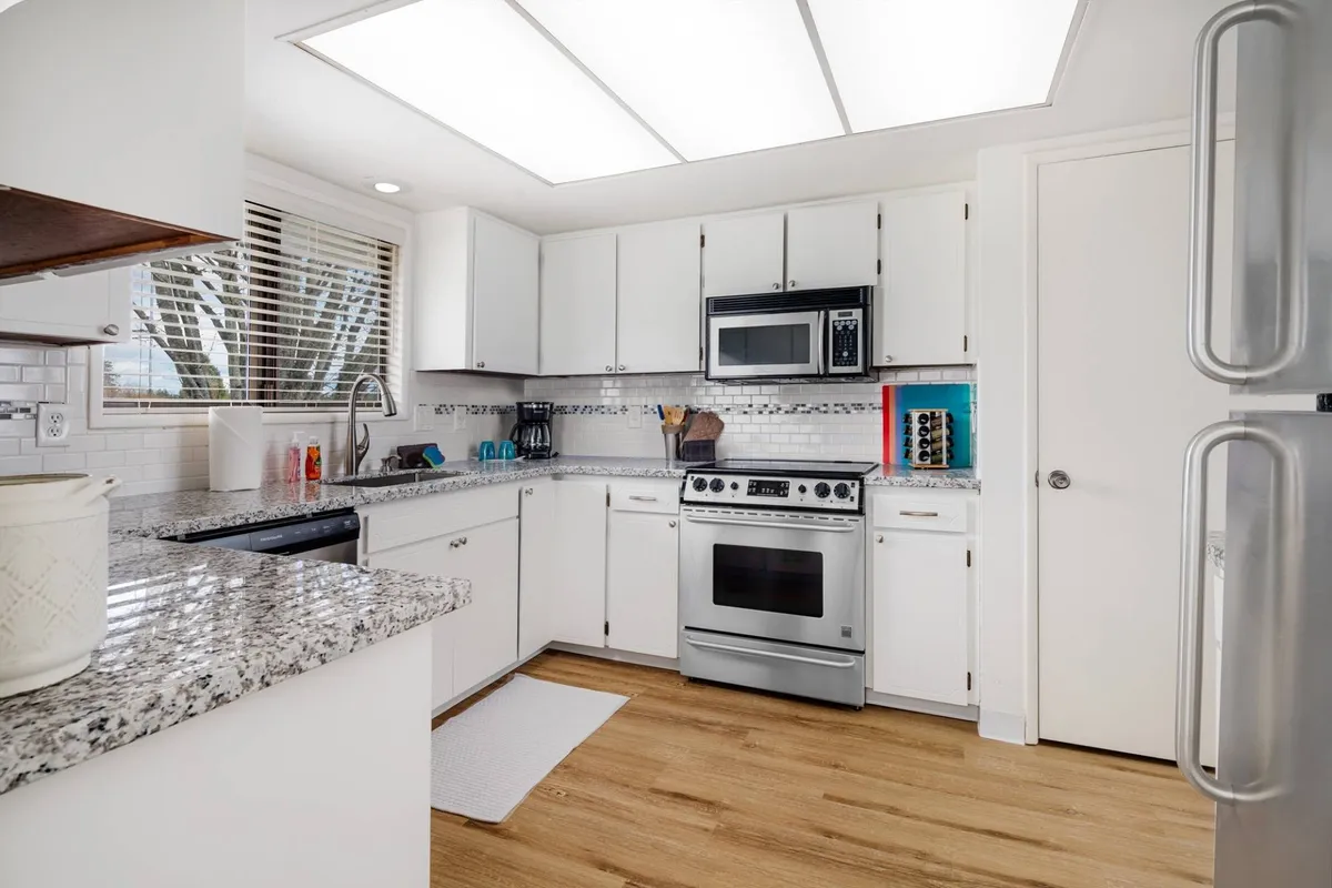 A bright, inviting kitchen featuring granite countertops, gleaming stainless steel appliances, and crisp white cabinetry. Sunlight pours in through a window, creating a cheerful atmosphere perfect for both cooking and gathering. The setup encourages family meals and celebratory occasions around the adjoining dining area.