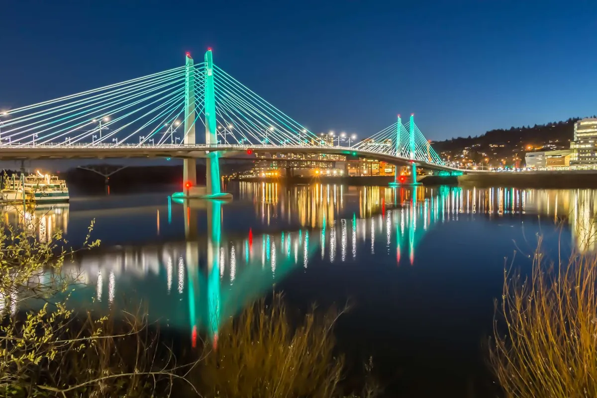This exterior image features a scenic bridge with its reflection shimmering on the water, set against a backdrop of city lights. The setting is calm and inviting, suggesting a peaceful outdoor environment ideal for walking, photography, and enjoying the surrounding natural beauty.